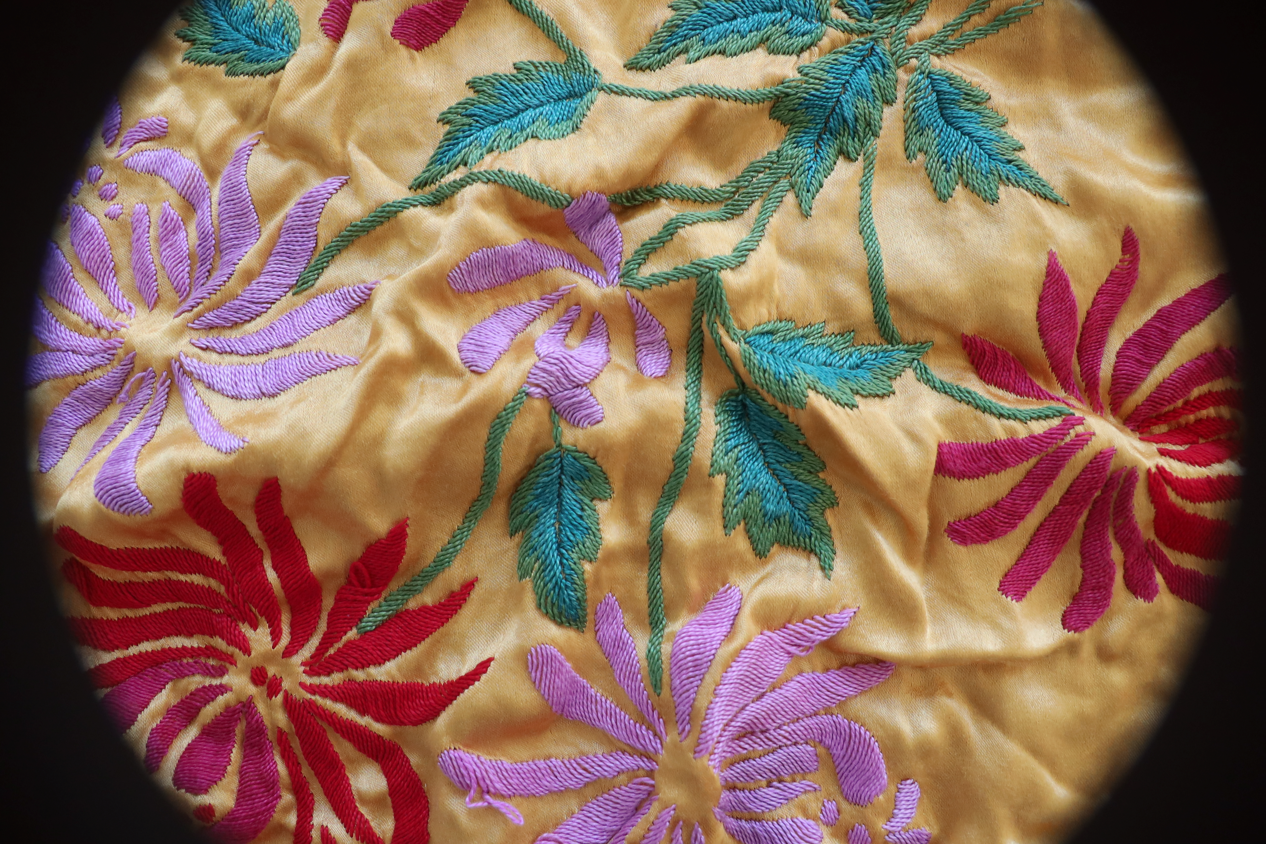 Trzy, stopniowe ujęcia od ogółu do szczegółu ujęcia na sfotografowany bezcieniowo na białym tle czarny, plastikowy neseser z napisem Polskie Linie Lotnicze LOT. W środku zwitek gazet oraz złota serweta wyszywana w różnokolorowe kwiaty.